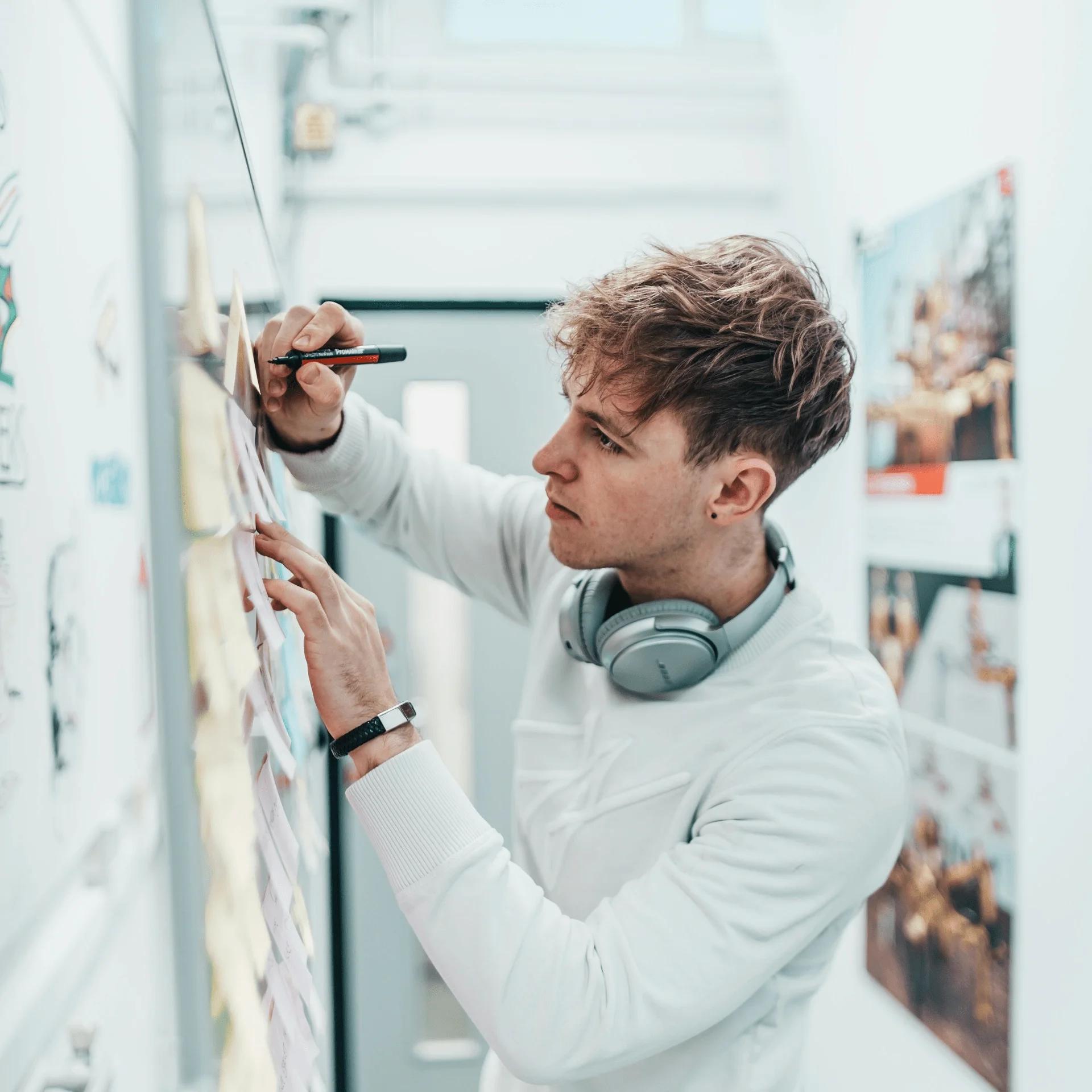 Junger Mann mit Kopfhörern zeichnet an White Board.