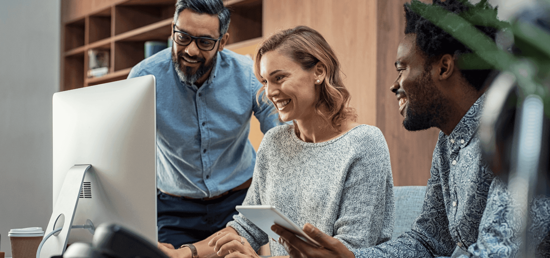 Three workers sitting smiling in front of a computer screen.