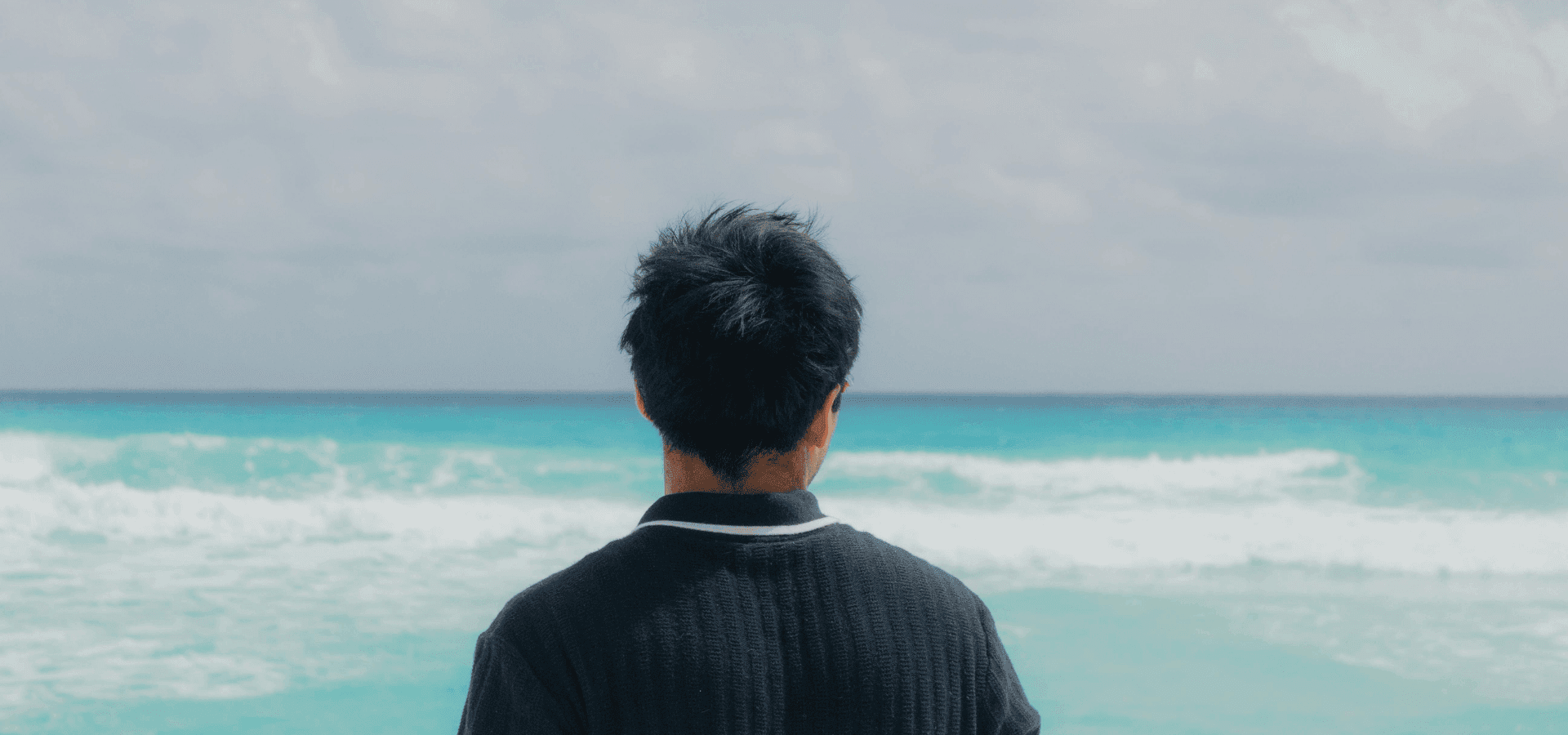 Ein Mann steht vor dem Meer, hinter ihm brechen sich blaue Wellen. Er gönnt sich eine Auszeit vom Arbeitsalltag.